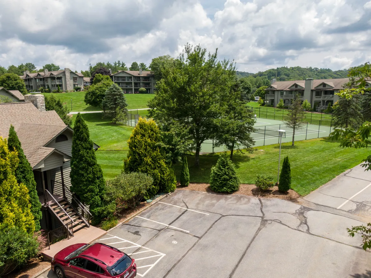 This exterior image features tennis courts surrounded by lush green trees with residential buildings visible in the background, creating an inviting outdoor recreational scene.