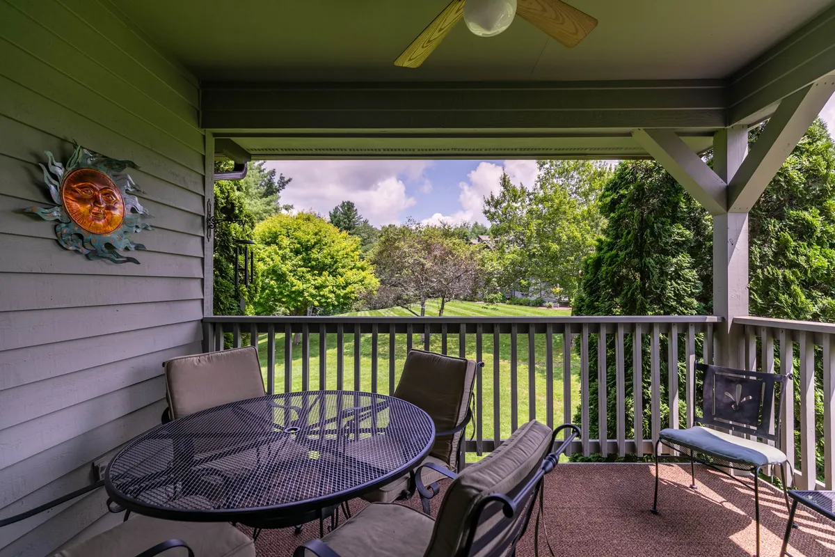 A covered patio with a table and chairs is shown, set beside lush greenery and decorative sun wall art. The overhead fan adds comfort for all-season enjoyment, and the space is inviting for morning coffee or evening relaxation while overlooking the resort grounds.