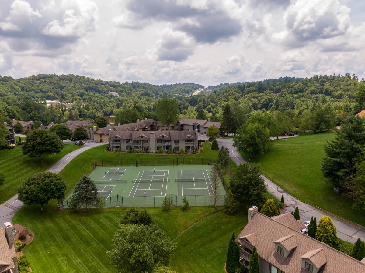 This image shows a set of well-maintained tennis courts nestled among residential buildings and surrounded by vibrant greenery. The setting conveys a sense of community energy and recreational opportunity, with ample space for outdoor gatherings and friendly matches.
