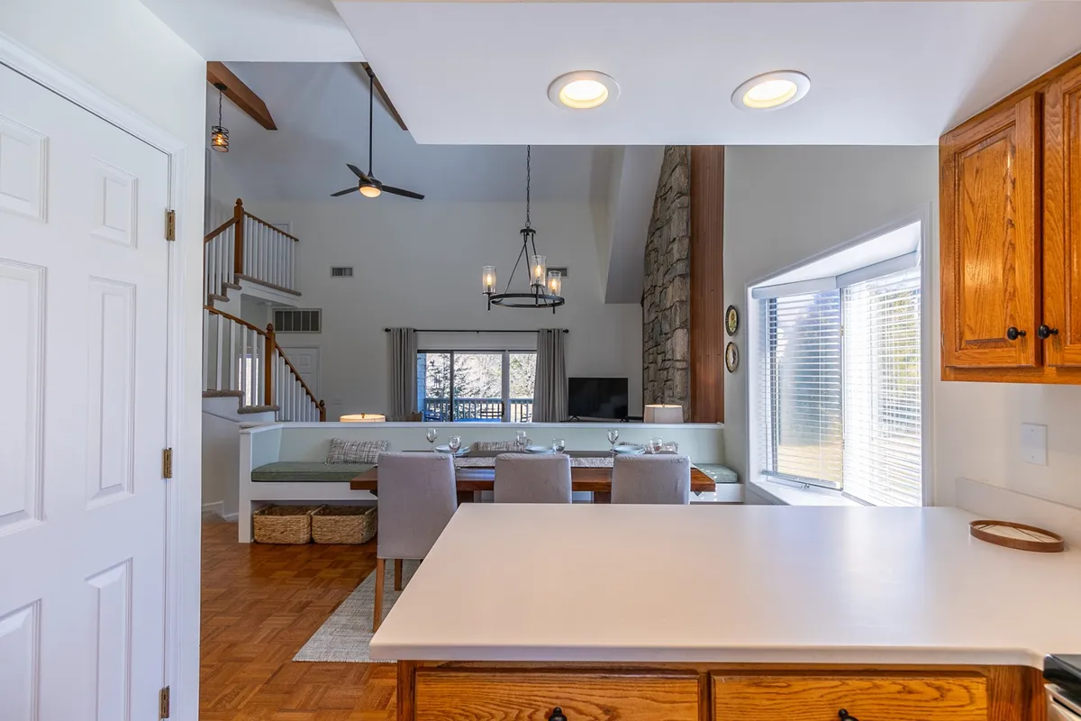 A bright, open-concept space featuring a kitchen island, adjacent dining area, and a stone fireplace. Large windows bring in ample natural light, and the arrangement supports easy movement between cooking, dining, and relaxing.