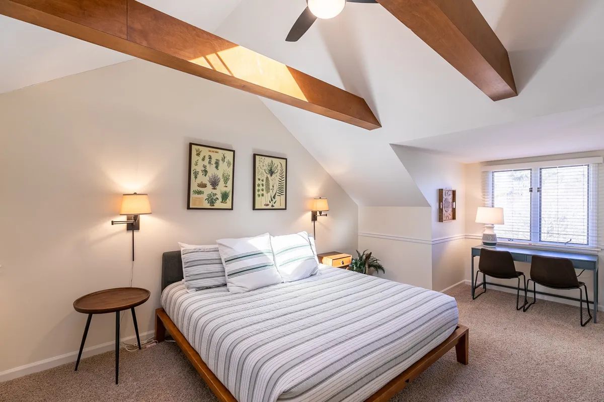 A serene and inviting bedroom with a comfortable bed, a window letting in natural light, stylish wall art, and a dedicated desk nook perfect for work or journaling. The tranquil environment emphasizes relaxation and privacy, ideal for a king suite.