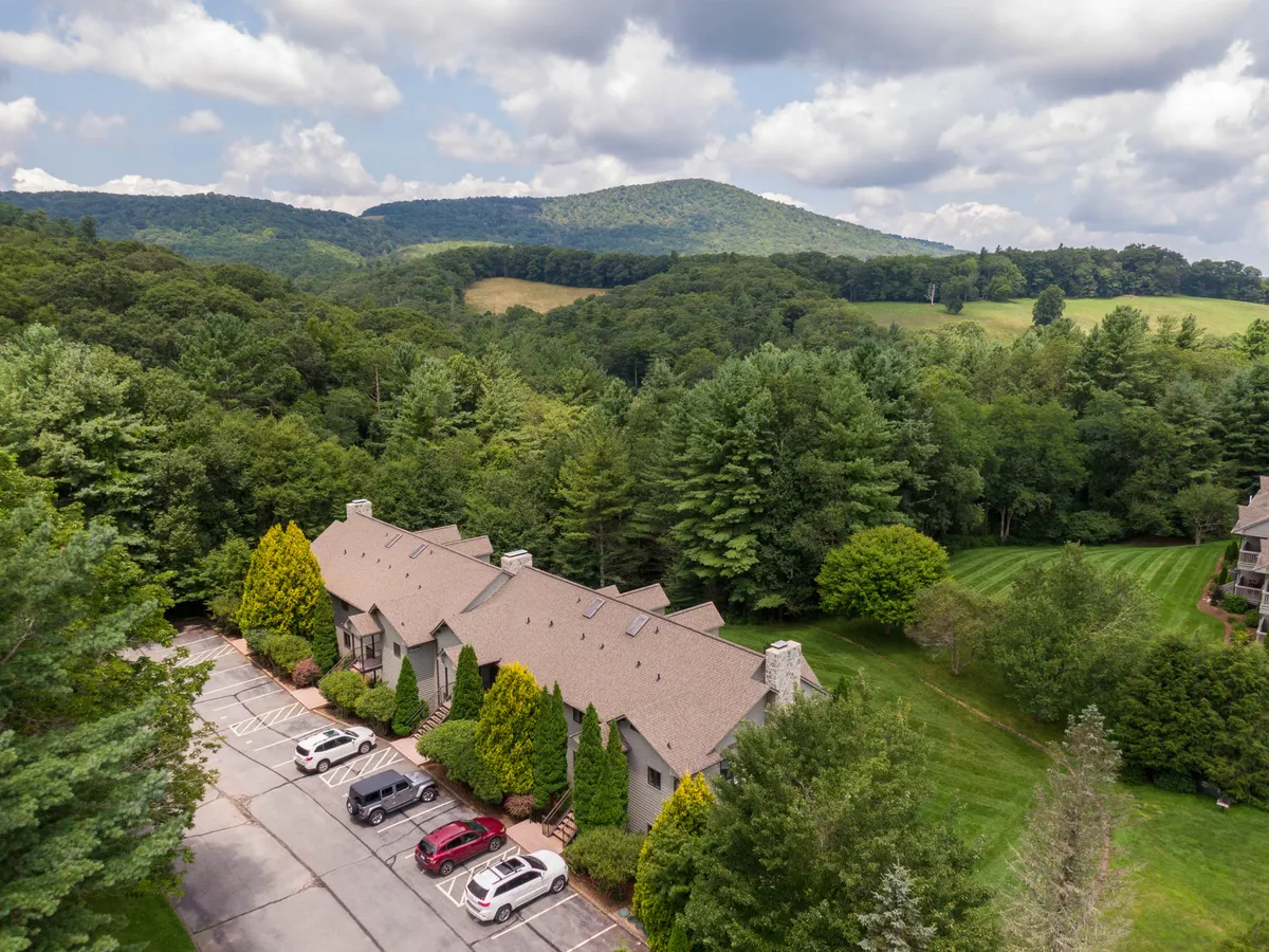 An outdoor scene highlighting the mountain range, lush greenery, and the resort's architecture. The visible parking area suggests convenient arrival and proximity to amenities, while the mountains evoke opportunities for hiking and outdoor exploration.