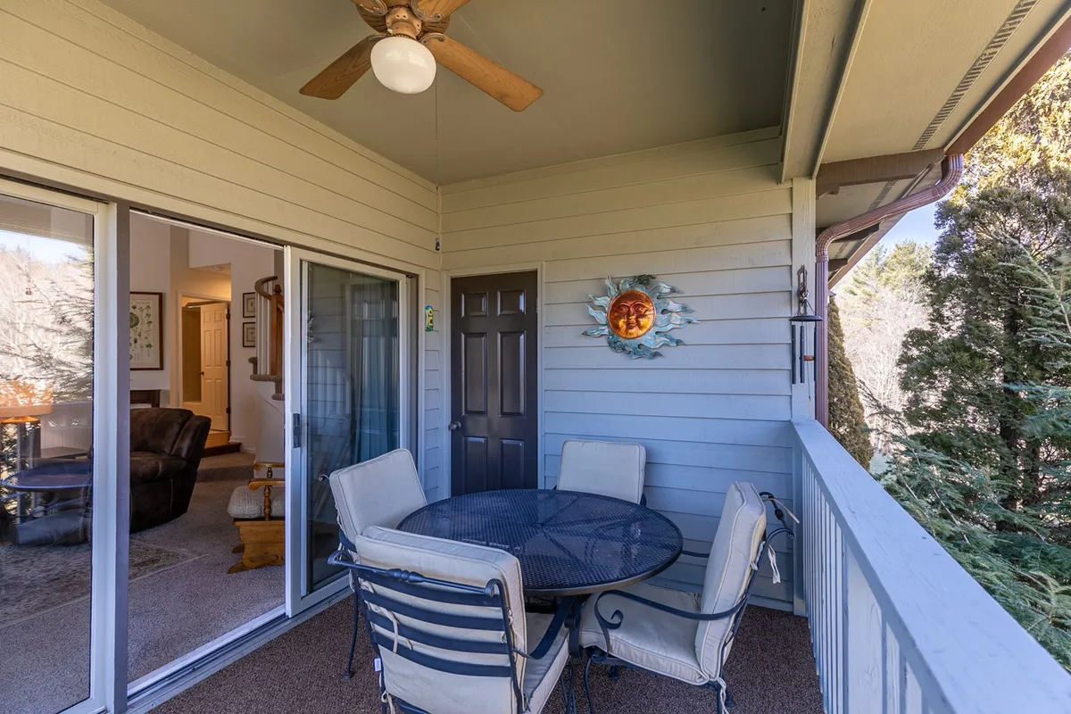 An outdoor covered patio features a round table with chairs, decorative wall art, and a ceiling fan, set against the backdrop of lush greenery. The atmosphere is tranquil and perfect for enjoying meals outdoors.